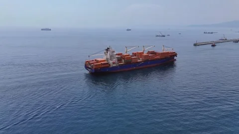 Aerial approaches huge container ship with cargo boom cranes on deck 스톡 동영상 345011182