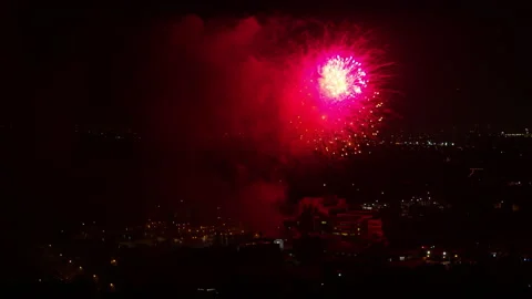 Aerial Backward Shot Of Beautiful Exploding Fireworks Against Clear Sky In City Stock Footage 169489700