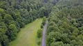 Aerial backwards flight shot small street and meadow within woodlands (2/4) 4k or 4k+ Resolution