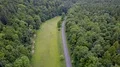 Aerial backwards flight shot small street and meadow within woodlands (3/4) 4k or 4k+ Resolution
