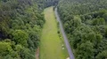 Aerial backwards flight shot small street and meadow within woodlands (4/4) 4k or 4k+ Resolution