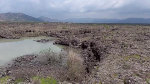 Aerial basalt lava plain with lake water and dark - Solidified and Dark Terrain Stock Footage 339405738