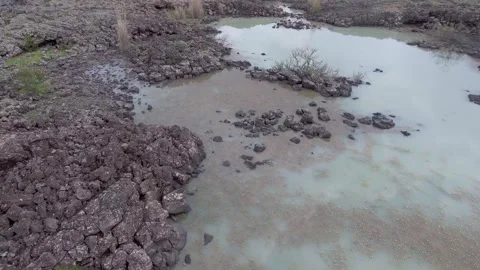 Aerial basalt lava plain with lake water and dark volcanic rock reveals - Crust Stock Footage 339406379