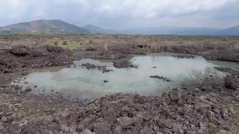 Aerial basalt lava plain with lake water and dark - Surface and Ancient Geology Stock Footage 339407007