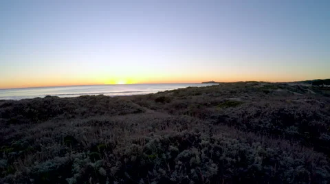Aerial birds eye view of camera flying over sand dunes then sunset over ocean Stock Footage 60942880