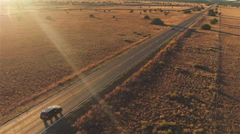 AERIAL: Black SUV car driving along empty country road at golden summer sunset Stock Footage 62516142