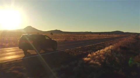 AERIAL: Black SUV car driving along empty country road at golden summer sunset Stock Footage