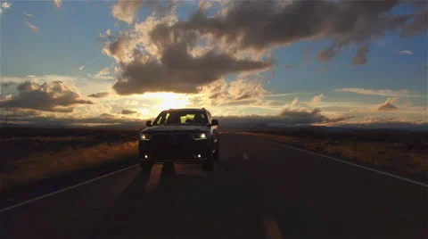 AERIAL: Black SUV car driving along the empty countryside road at golden sunset Stock Footage