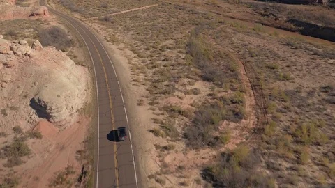 AERIAL: Black SUV car driving along the winding empty road through canyon valley Stock Footage