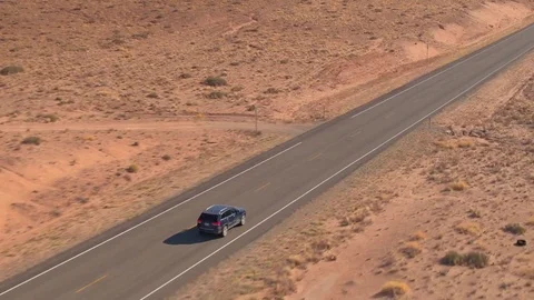 AERIAL: Black SUV jeep driving along the straight empty road through dry desert Stock Footage