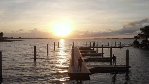 Aerial of boat dock and people fishing with sunset ahead Stock Footage 128714919