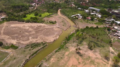 Aerial brown river bend through tropical village fields palms and dry flats Видео 336699325