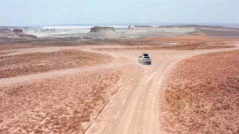 Aerial camera tracking car driving away rear view toward forked dirt junction Stock Footage 334025818
