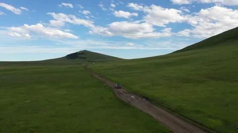 Aerial Car Driving Through Rolling Green Hills Under a Cloudy Sky Vidéo 109530475