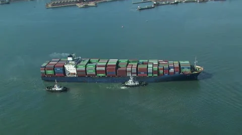 Aerial of cargo ship assisted by tug boats and fully loaded with containers Stock Footage