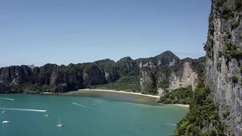 Aerial cinematic view: Tall cliffs, tropical emerald sea, many boats and beach Stock Footage 73062336