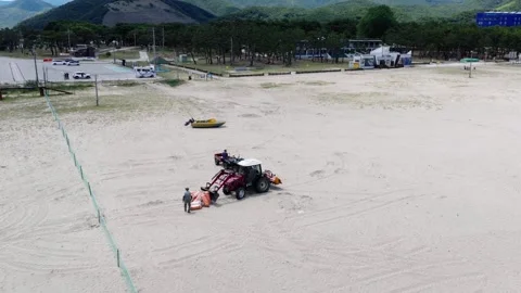 Aerial Circle Shot of Workers and Tractor on a Beach Stock Footage 313108533
