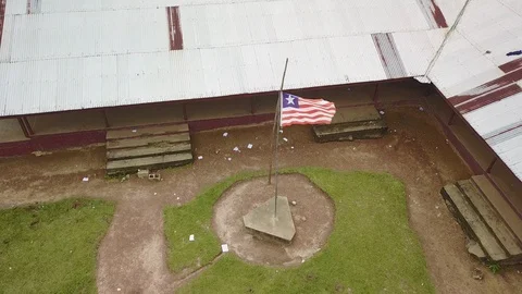 Aerial Circling Third World School with Liberian Flag Blowing in Wind 스톡 동영상 101621119