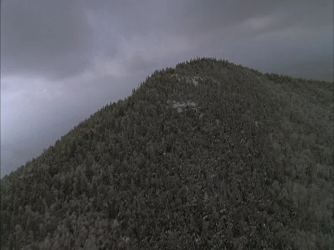 Aerial climbs up tree covered mountainside in snow then over the top. Stock-Footage 86750531
