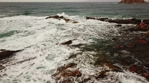 Aerial close approach from above . Rough sea, waves moving on the rocks. Stock Footage 100332237