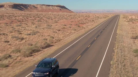 AERIAL CLOSE UP: Black SUV car driving on empty road through vast desert valley Stock Footage