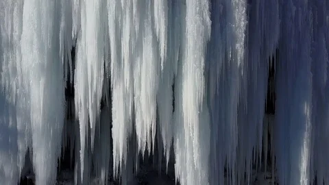 AERIAL CLOSE UP: Flying around waterfall frozen into icicles in sunny winter Stock Footage