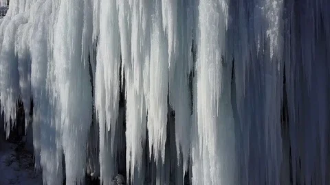 AERIAL CLOSE UP: Flying around waterfall frozen into icicles in sunny winter Stock Footage
