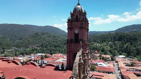 Aerial close orbit of a pink stone church tower above a red roofed town with Stock Footage 346015514