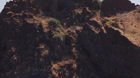Aerial close up of reddish brown cliffs rising from sparse vegetation revealing Stock Footage 308407704