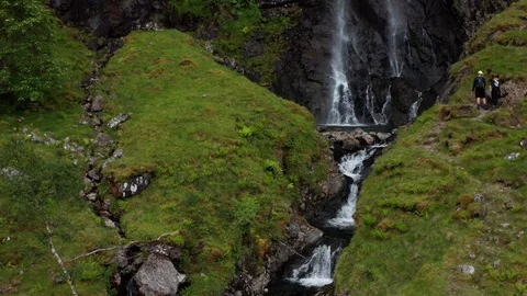 Aerial close in shot of hikers admiring the beautiful waterfall in Scotland 스톡 동영상 116043053