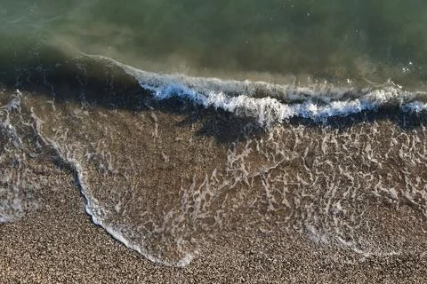 Aerial close up top down view of sea foam spreading on pebble beach. Фото