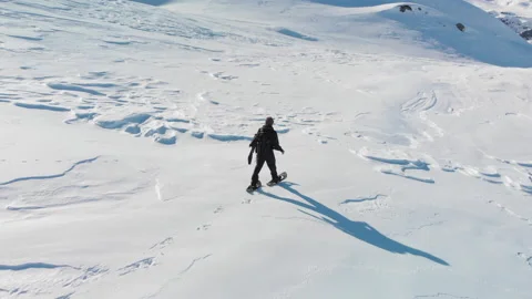 Aerial close view of man walking through snow on snowshoes on snowy mountain Stock Footage 145889166