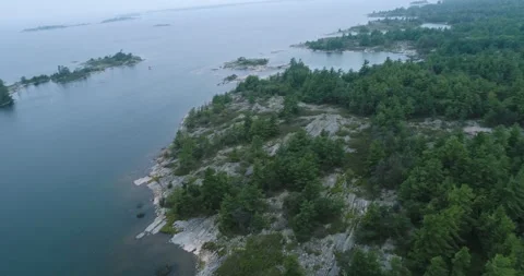 Aerial On Cloudy Day Over Smooth Glacier Rock And Pine Northern Lake Shoreline Video stock 188475686