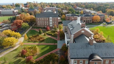 Aerial of college campus in autumn, brick buildings tower over autumn Stock Footage