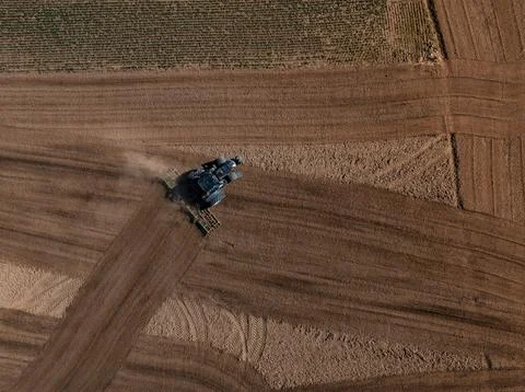 Aerial combine harvester cuts patterned wheat fields at sunset Stock Photos