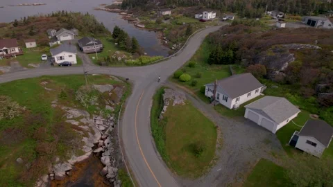 Aerial of Cyclist Biking Through Small Fishing Village, Ocean Coastline Stock Footage 191654663
