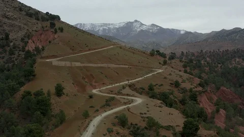 An aerial of cyclists climbing switchbacks towards a ridge of snowy peaks. Stock Footage 127038966
