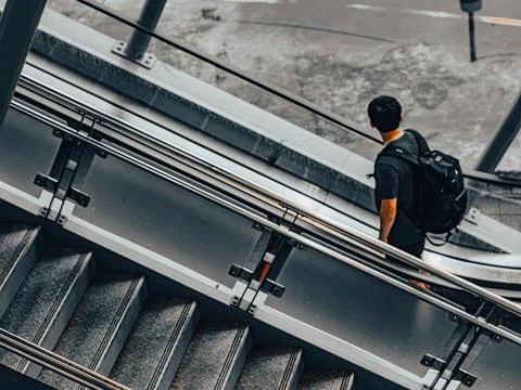 Aerial Diagonal View of Man with Backpack Descending Station Escalator 库存照片