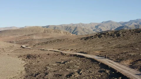 An aerial of a dirtbike stopped on a thin path cutting through a barren desert. Stock Footage