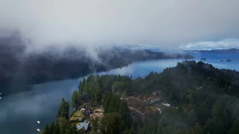 Aerial dolly in through low clouds revealing snowy mountains and Nahuel Huapi 動画素材 334177732