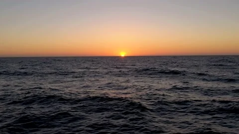 Aerial dramatic flight above ocean waves while the sun sets below the horizon in Stock Footage 218350526