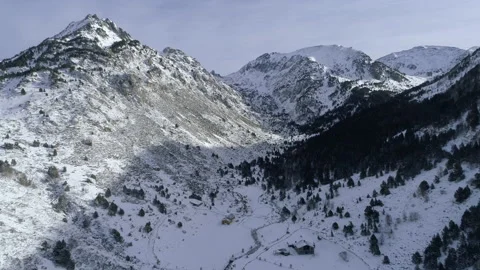 AERIAL DRONE BACKWARD SHOT THROUGH SNOWED VALLEY,ROCKY MOUNTAIN AND WOODS Stock Footage 130339239