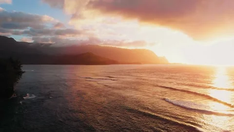 Aerial drone camera captures pink sunset over ocean waves and mountains in Kauai Stock-Footage 136428152