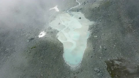 Aerial drone flight in the clouds over turquoise glacial lake in the mountains Stock Footage 215883428