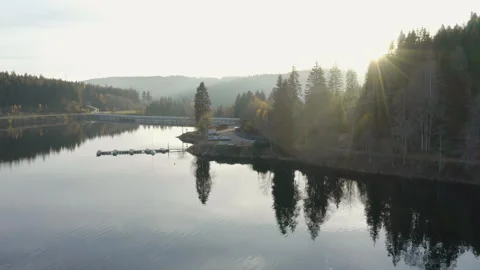 Aerial drone flight over a mountain lake at sunset with sun rays through pines Stock Footage 321125626