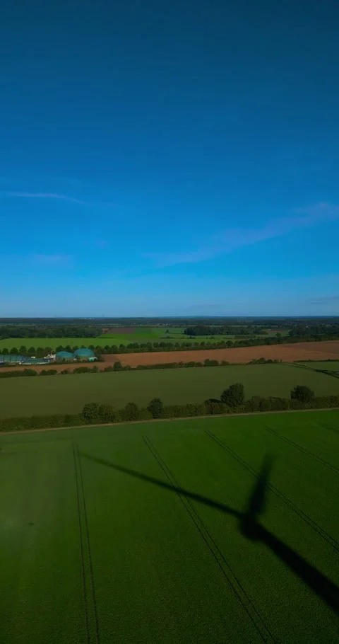 Aerial drone flight over open fields while a shadow of a wind turbine spins Stock Footage 253031817