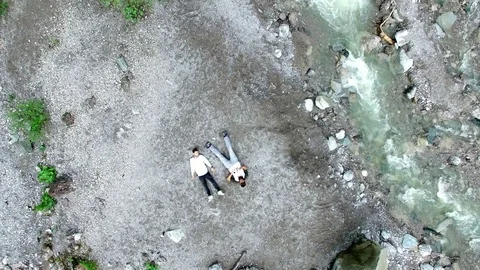 Aerial drone flight over two young guys lying on rocks next to a river in a Video stock 80543749