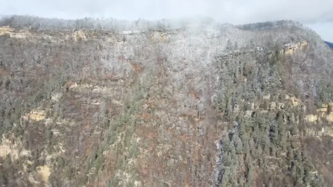 Aerial drone flight towards a snow-dusted rocky mountain cliff Stock Footage 337541753