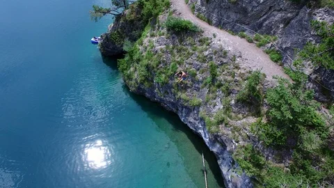 Aerial drone flight of young guy jumping into reflecting blue mountain lake on 스톡 동영상 91014690