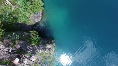 Aerial drone flight of young guy jumping back flip into blue mountain lake on Video stock 91014708